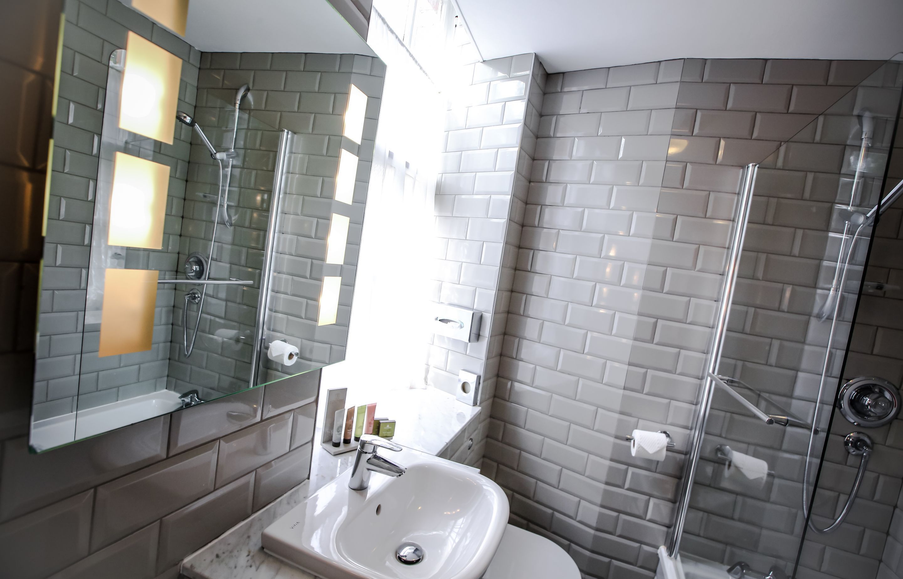 A modern bathroom with a glass shower enclosure, a white sink, and a mirror with integrated lighting.