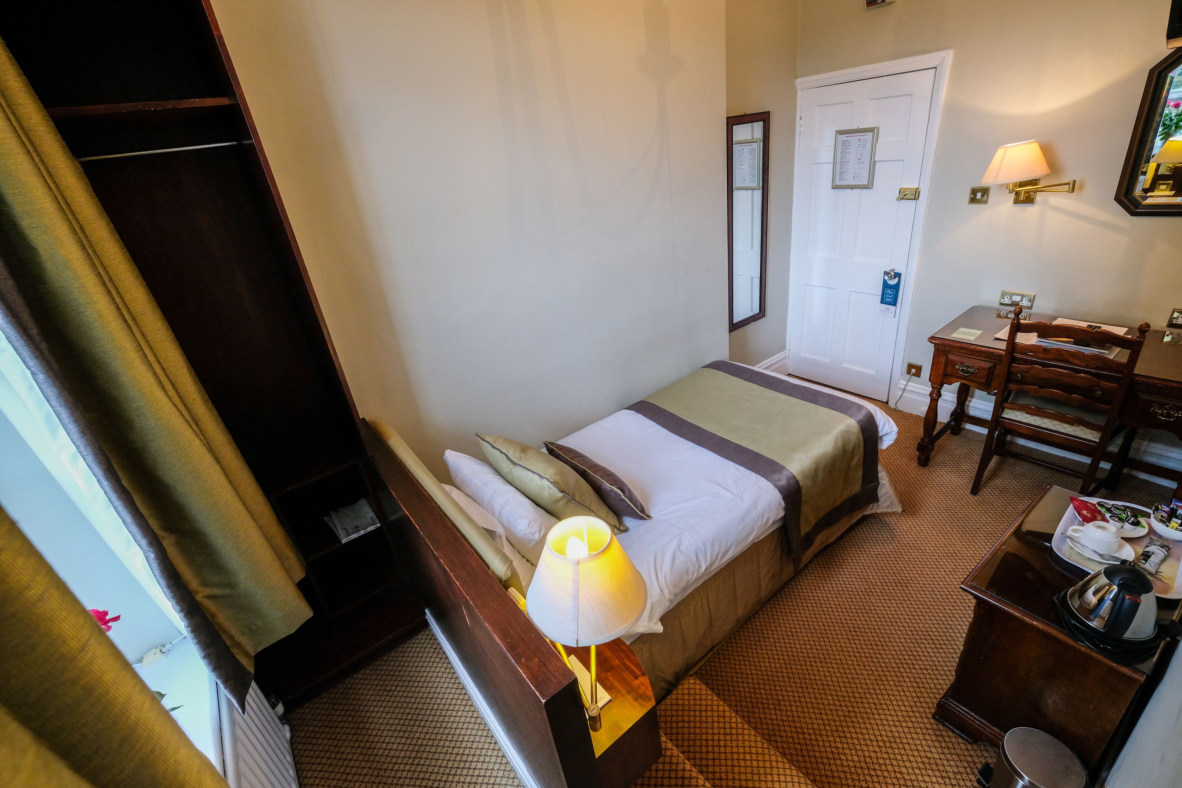 Una habitación de hotel con cama, escritorio, silla, lámpara y puerta.