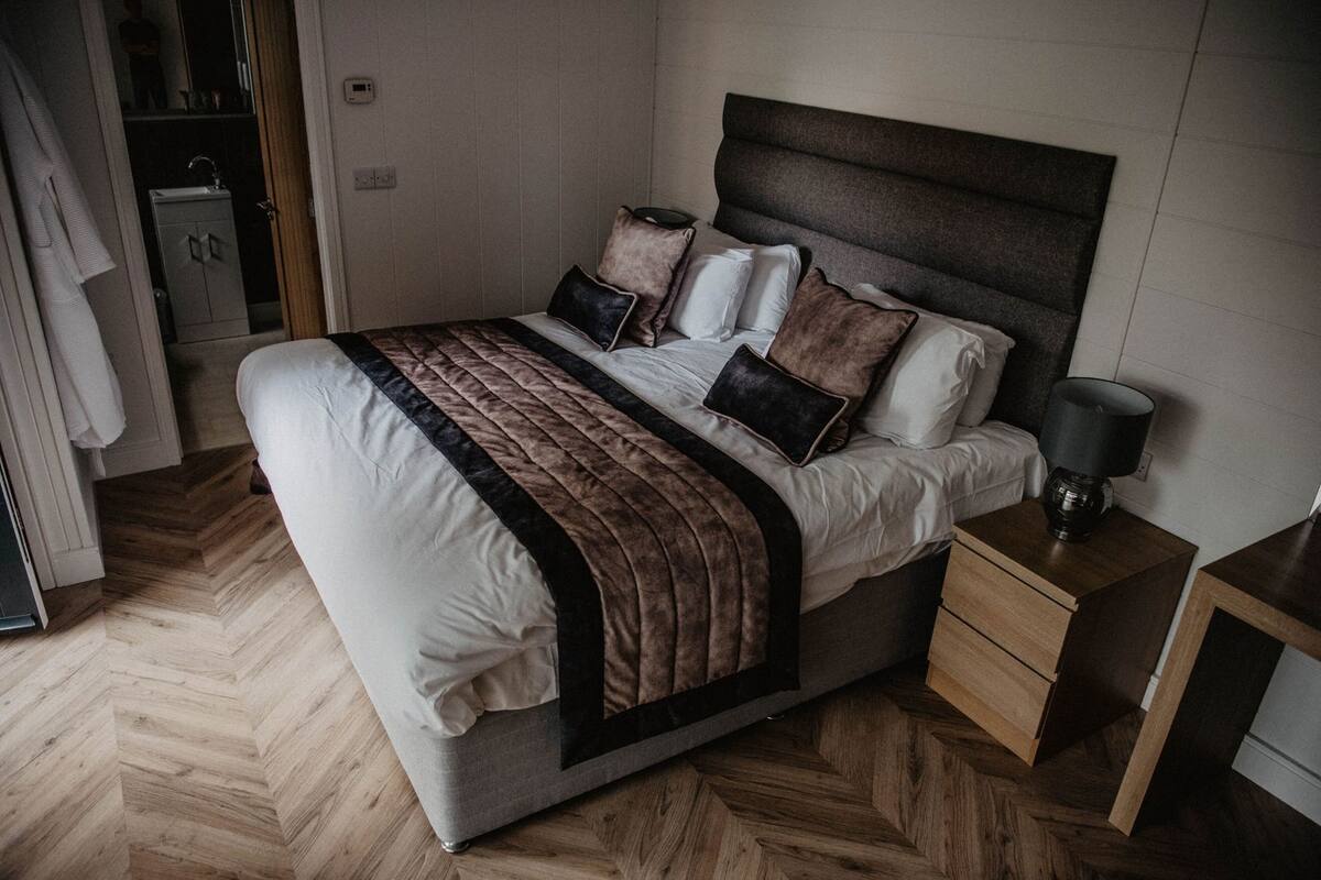 A bedroom with a bed, bedside tables, a nightstand, a lamp, a wardrobe, and a mirror.