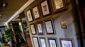 A hallway with framed artwork on the wall, potted plants, and a staircase. - Bowburn Hall Hotel (Durham)