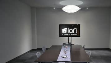 Un salón de conferencias con una larga mesa, sillas, una pantalla de televisión que muestra 'aloft' y una araña de cristal.