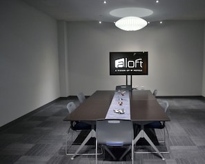A conference room with a long table, chairs, a TV screen displaying 'aloft', and a chandelier. - Aloft by Marriott Tulsa Downtown (Tulsa)