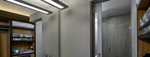 A modern bathroom with a shower, a vanity, and a shelf with toiletries. - Aloft by Marriott Tulsa Downtown (Tulsa)