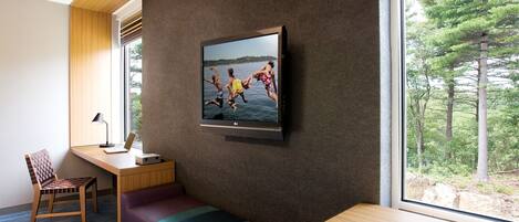 Una habitación moderna con un ventanal grande, televisor, escritorio y una banca.