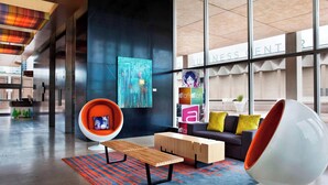 A modern lobby with a wooden bench, a white egg chair, and a coffee table. - Aloft by Marriott Tulsa Downtown (Tulsa)