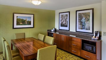 A dining area with a wooden table and four chairs, a kitchen with a microwave and coffee maker, and framed pictures on the walls.