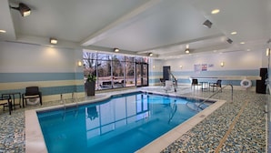 Une piscine intérieure avec des parois en verre transparent, un sol carrelé et un espace détente avec des chaises et une table.