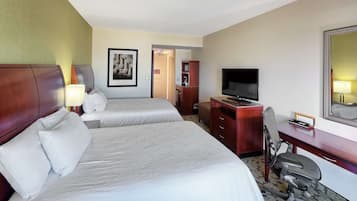 Habitación de hotel con dos camas, un escritorio con silla, un televisor y un cuadro en la pared.