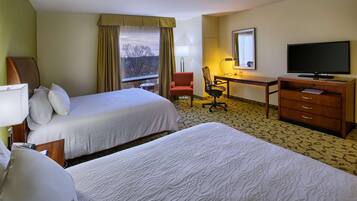 A hotel room with two beds, a desk with a chair, a television, and a window with curtains.