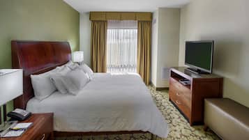 Una habitación de hotel con una cama, televisor, escritorio con lámpara y ventana con cortinas.