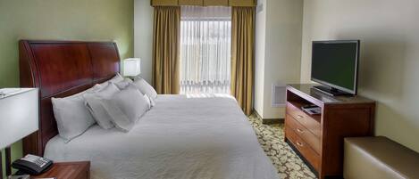A hotel room with a bed, a television, a desk with a lamp, and a window with curtains.