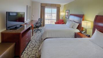 A hotel room with two beds, a desk with a TV, a chair, and a desk lamp.
