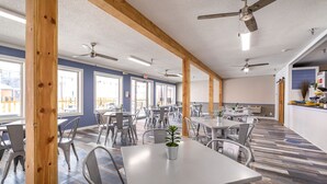 Un amplio comedor interior con varias mesas y sillas, ventiladores de techo y ventanas grandes.