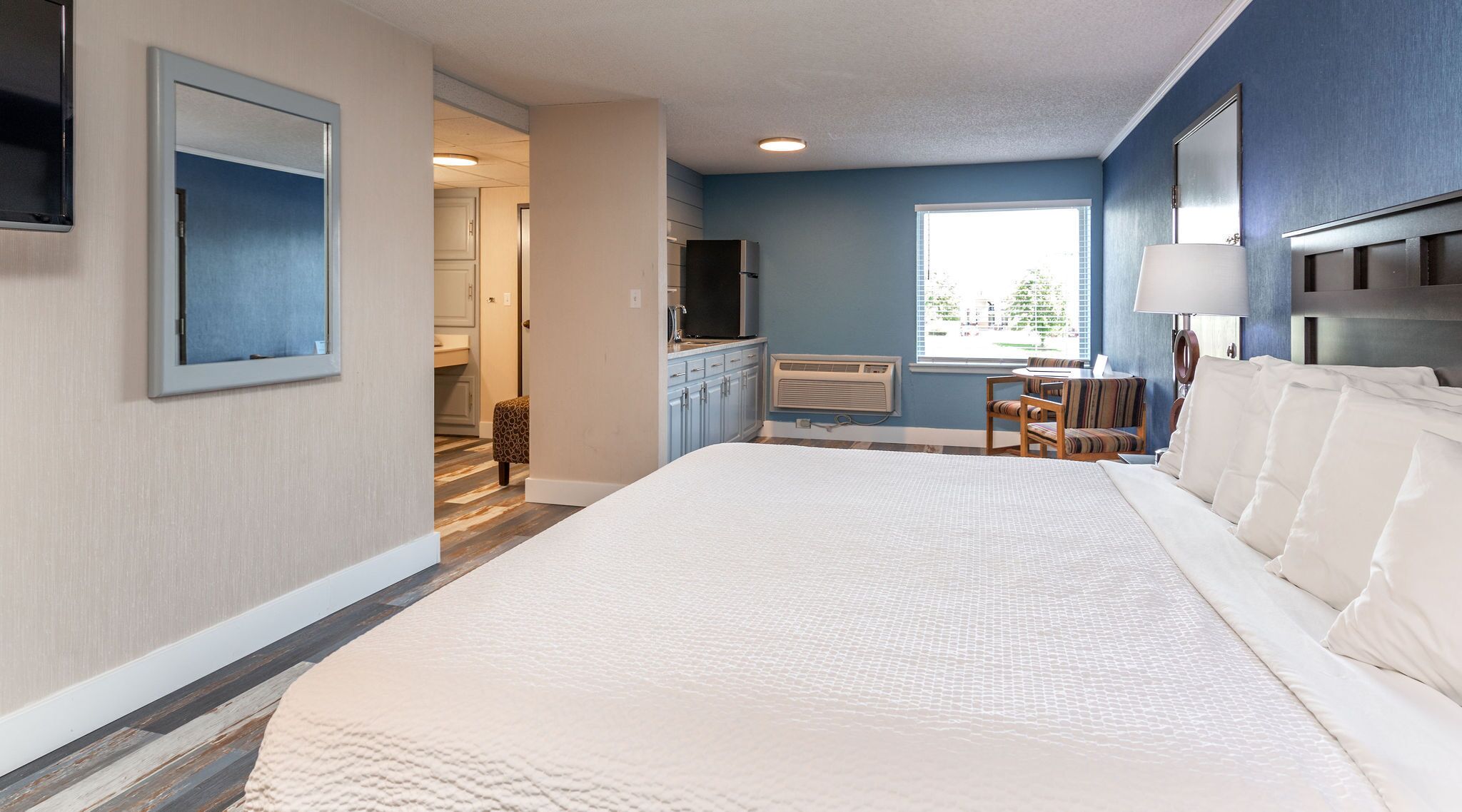 A hotel room with a large bed, a desk with a chair, a TV, and a window with a view of trees.