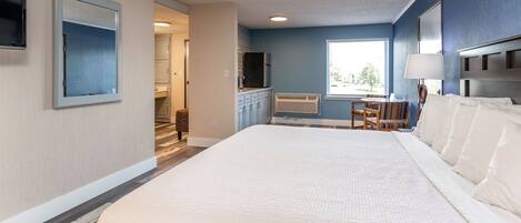 A hotel room with a large bed, a desk with a chair, a TV, and a window with a view of trees.