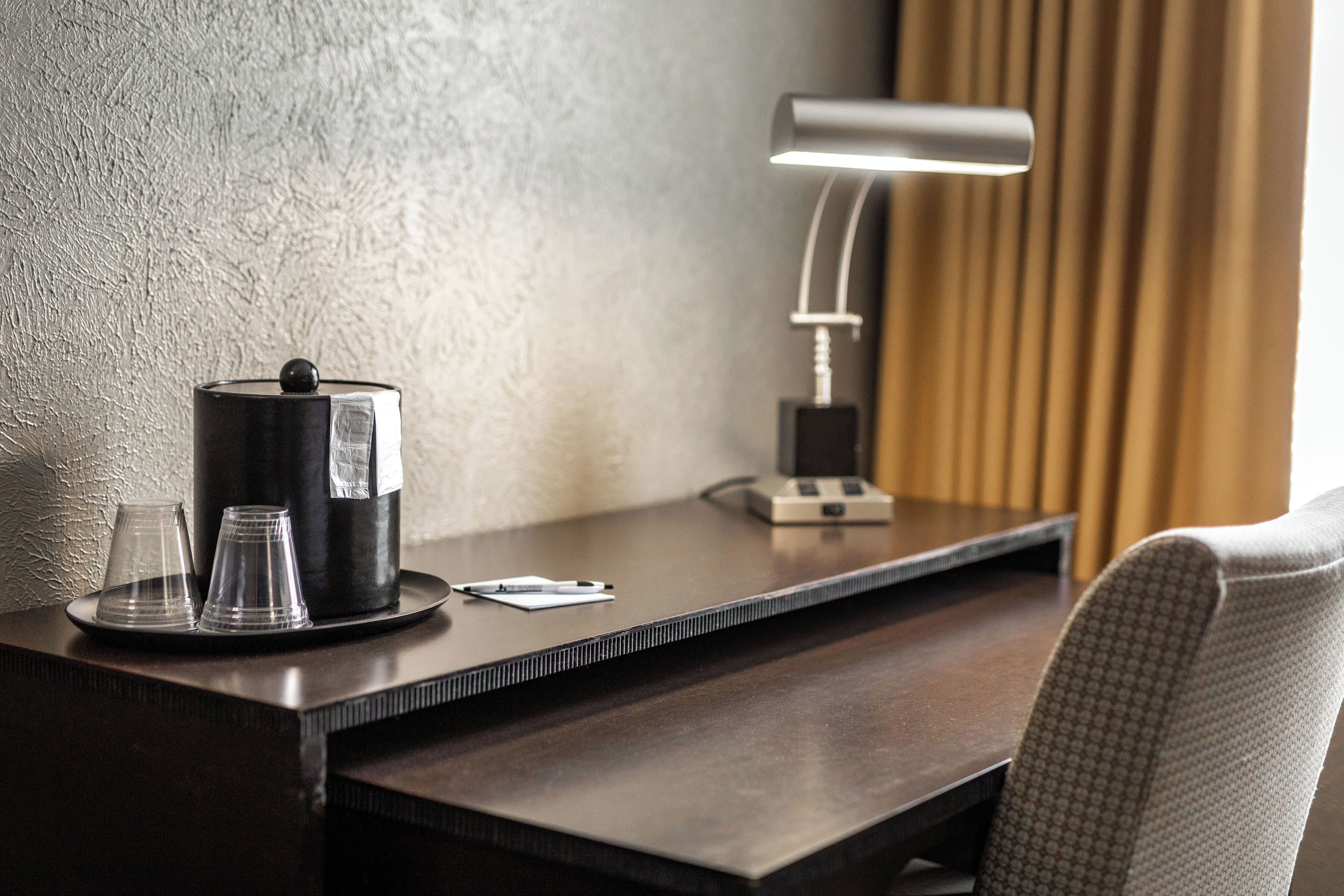 Un mostrador de hotel con cafetera, dos vasos y una lámpara.
