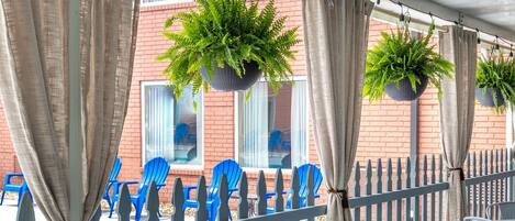 An outdoor patio area with tables and chairs, a brick building in the background, and hanging plants.