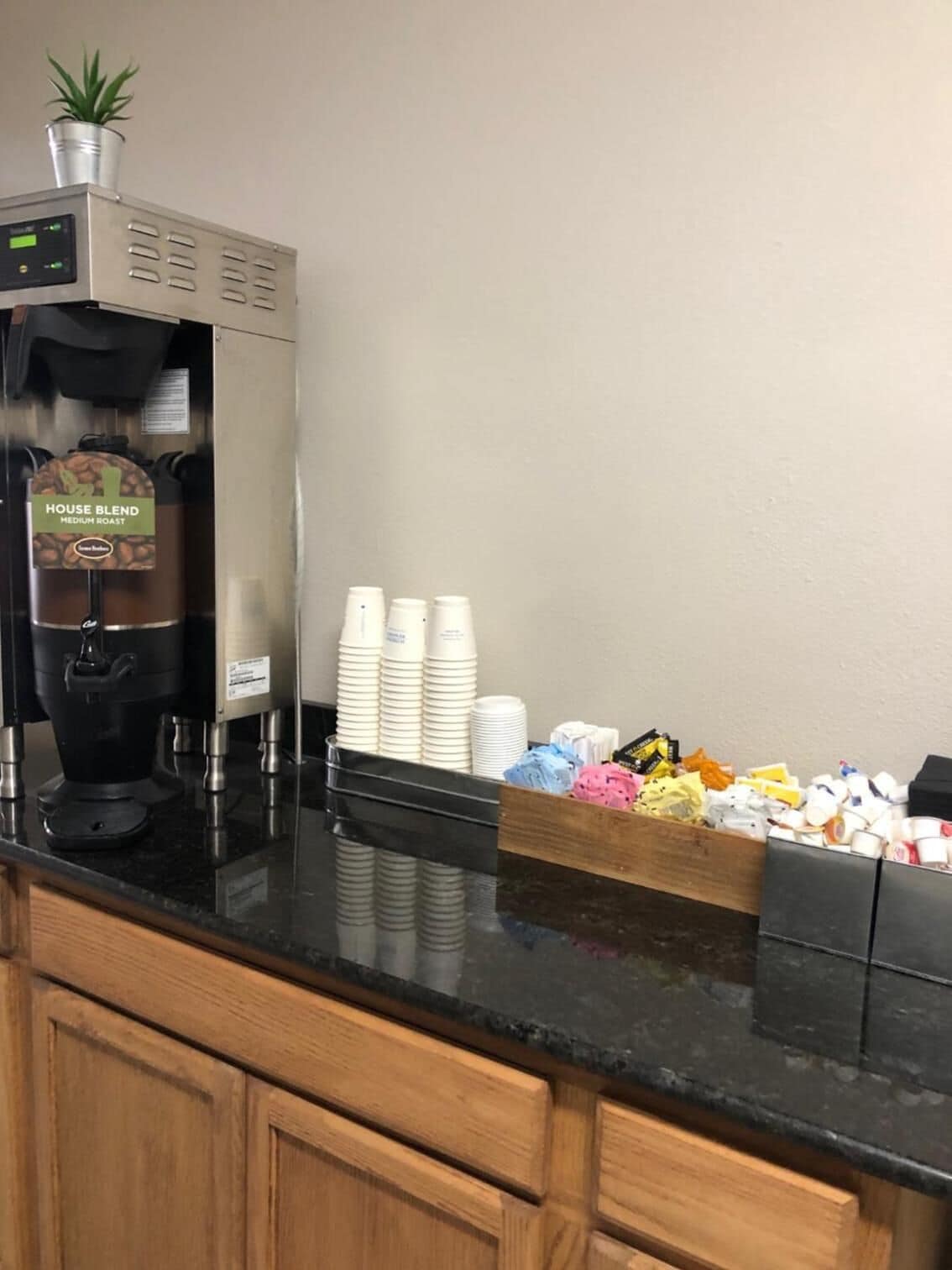 A coffee station with a coffee machine, disposable cups, and a tray of assorted snacks.
