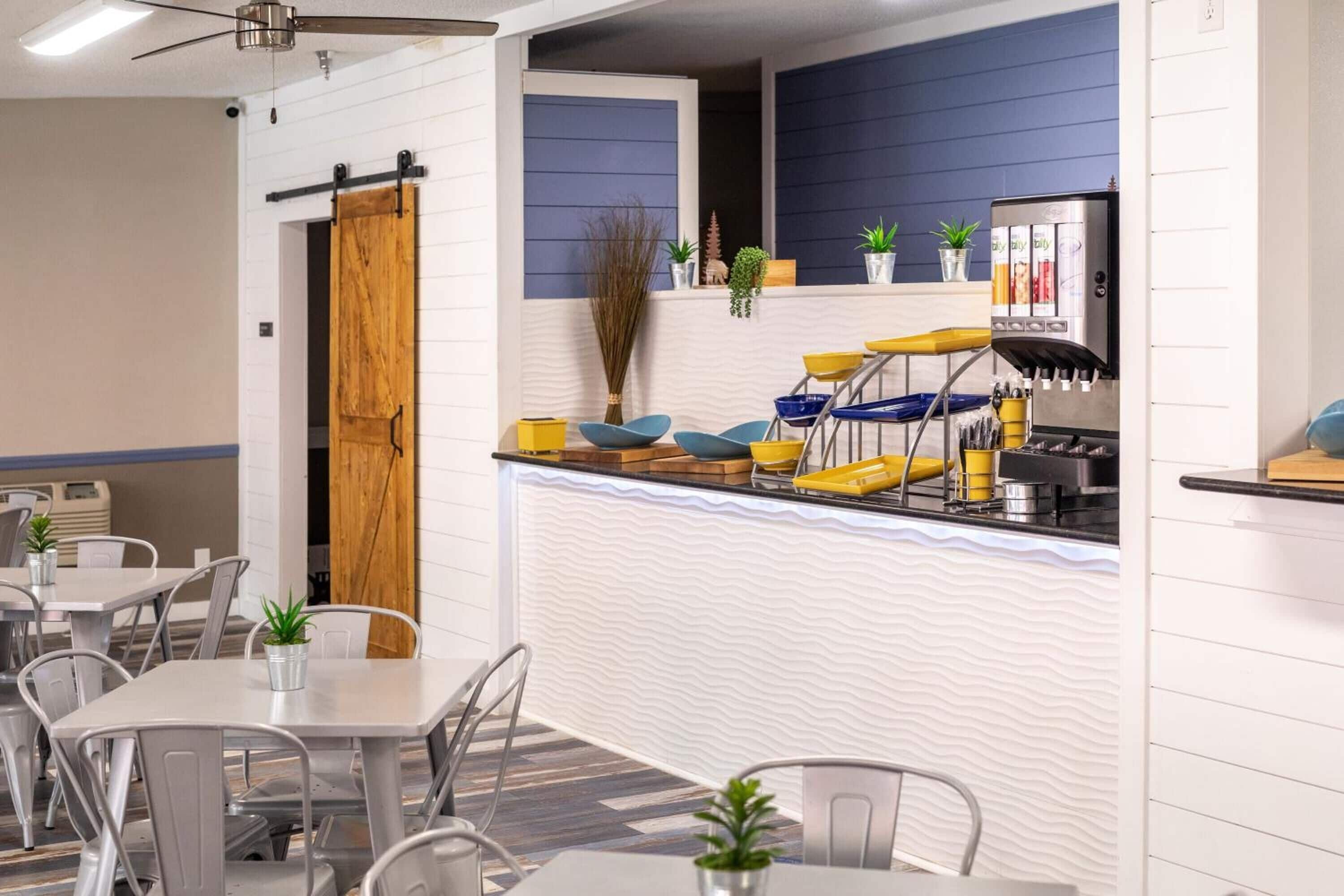 A modern cafe with a counter, seating area, and a ceiling fan.