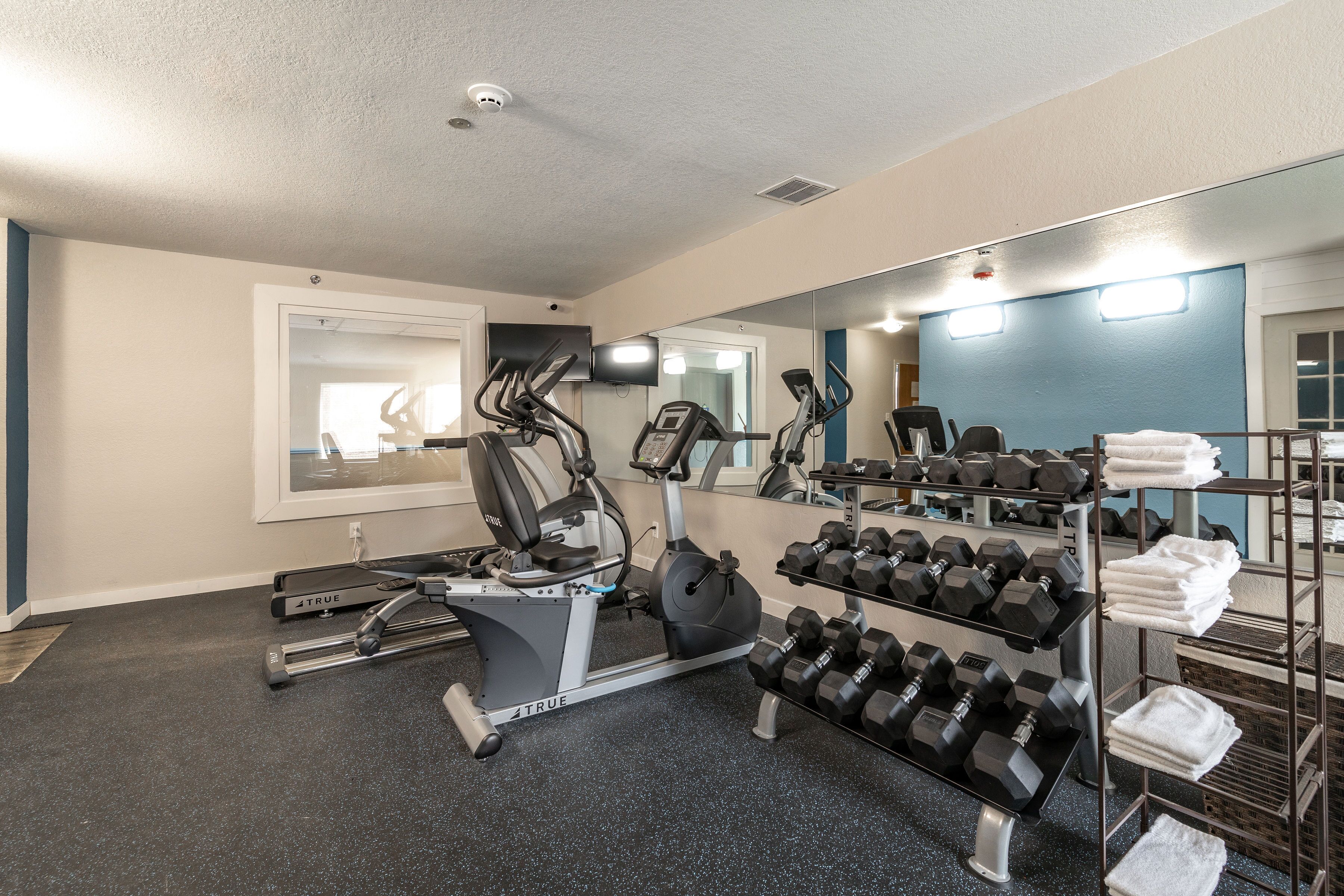A gym with exercise equipment, including treadmills and dumbbells, and a mirror reflecting the room.