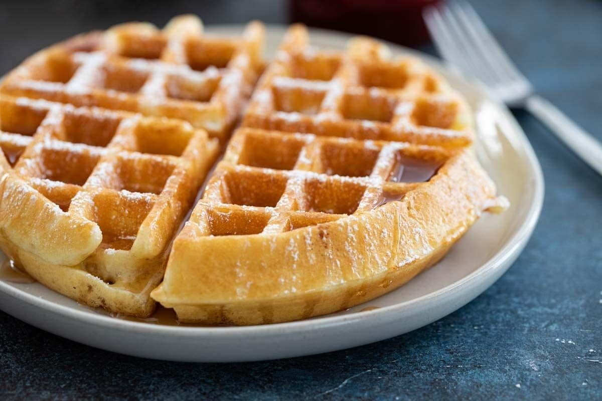 A plate of waffles with syrup, served on a white plate.