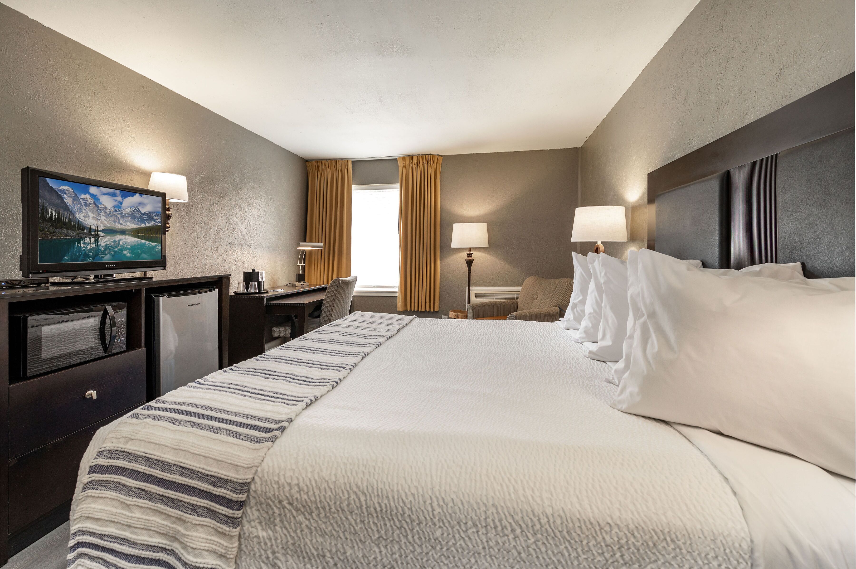A hotel room with a large bed, a flat-screen TV, a desk with a computer, a microwave, and a refrigerator.