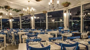 Un restaurante con varias mesas y sillas, ventanas amplias y plantas colgantes.