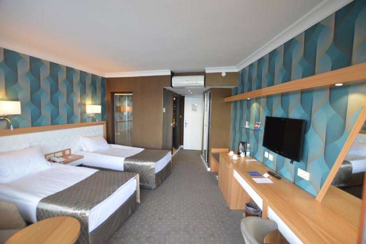 Habitación de hotel con dos camas, un escritorio, un televisor y un baño visible a través de una puerta abierta.