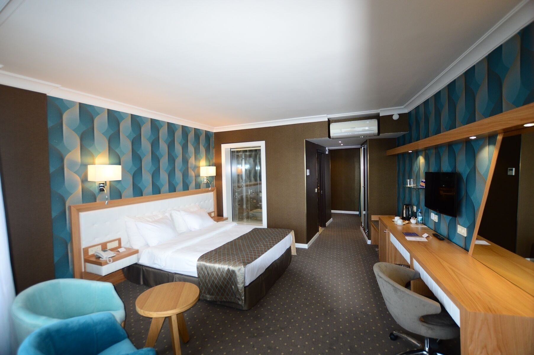 A hotel room with a bed, a desk, a chair, a TV, and a bathroom door.