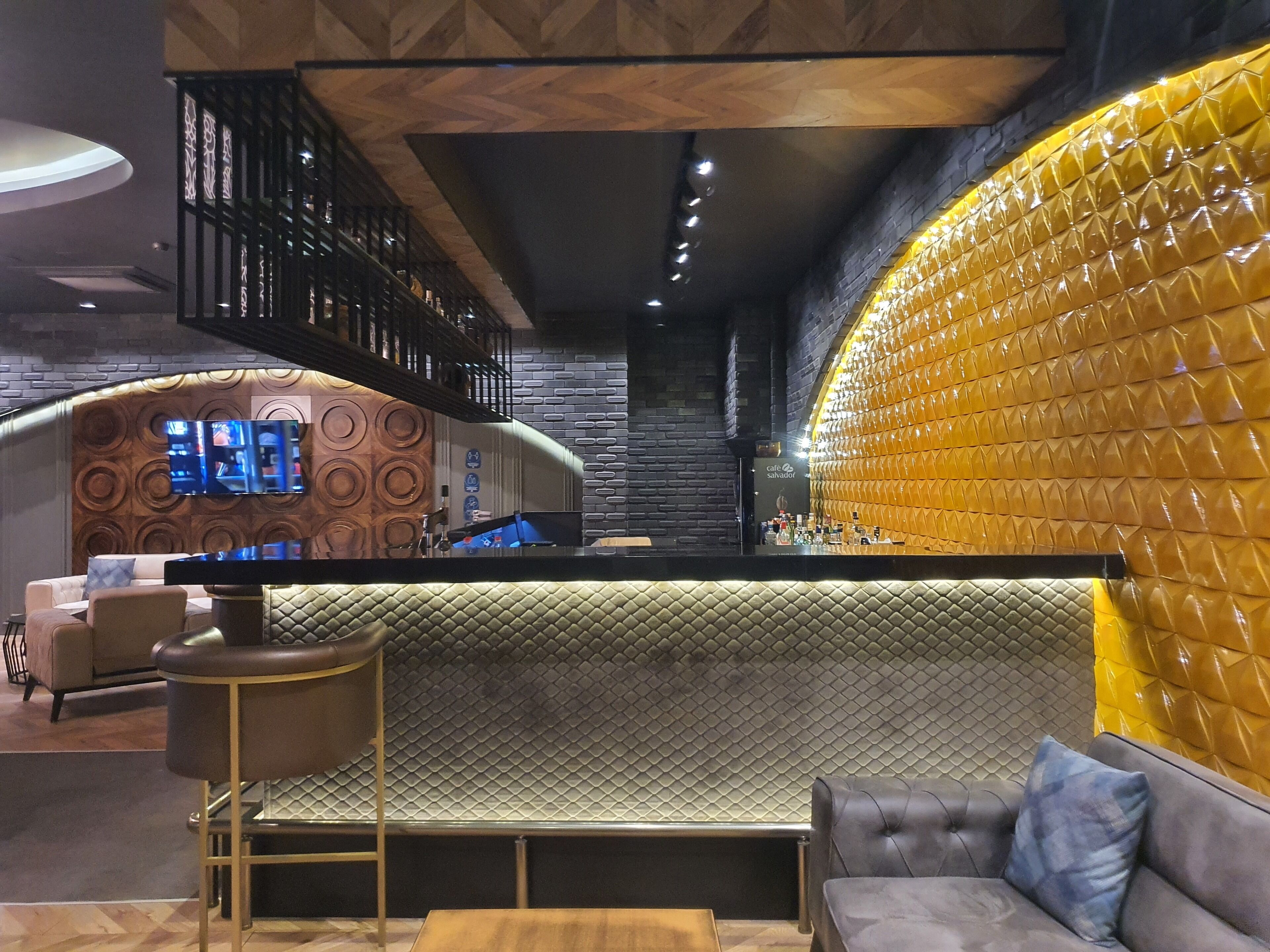A modern bar area with a counter, seating, and a TV screen.