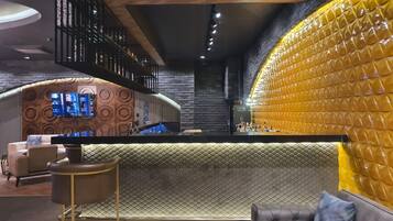 A modern bar area with a counter, seating, and a TV screen.