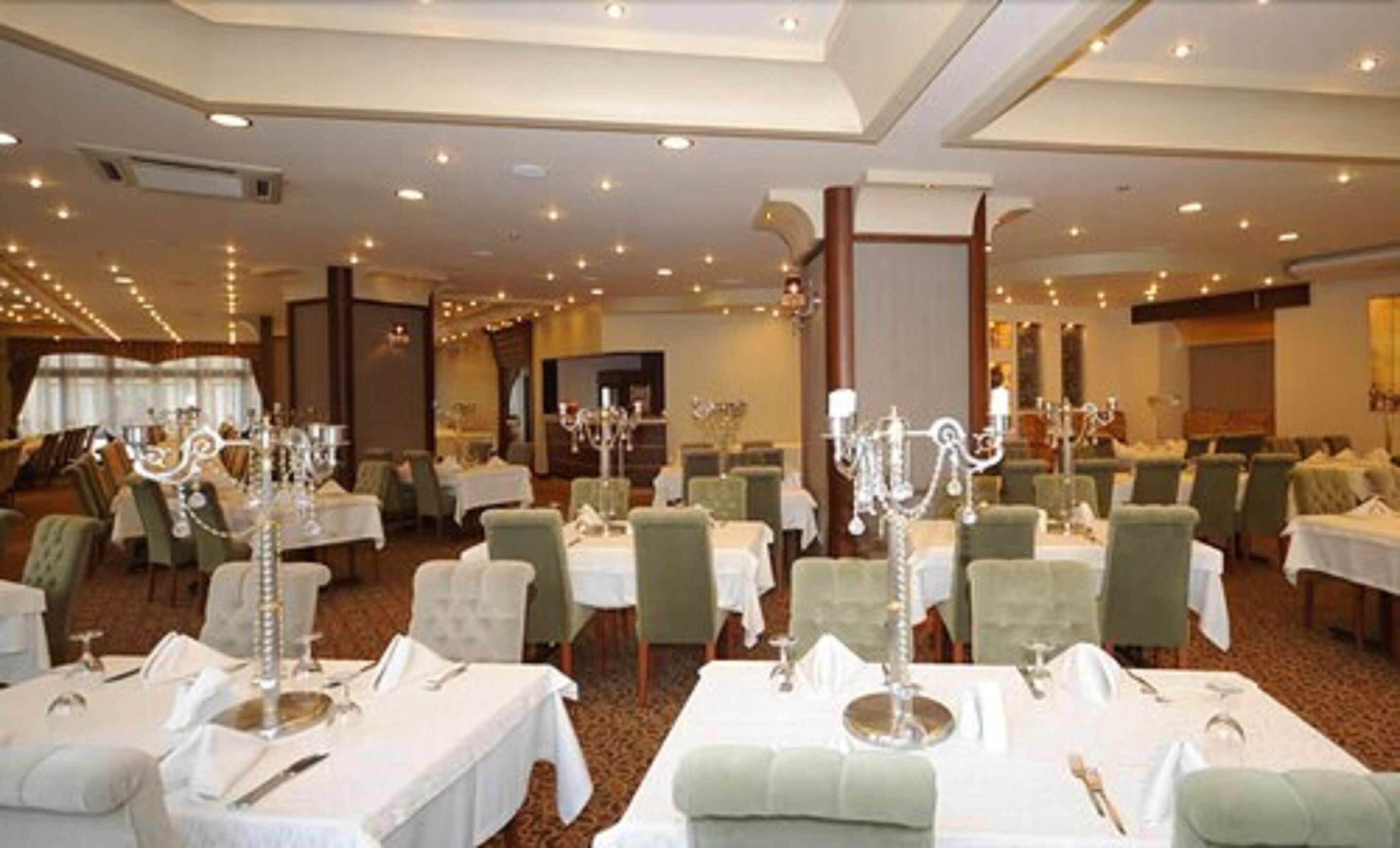 A banquet hall with round tables, each set with white tablecloths, silverware, and candelabras.