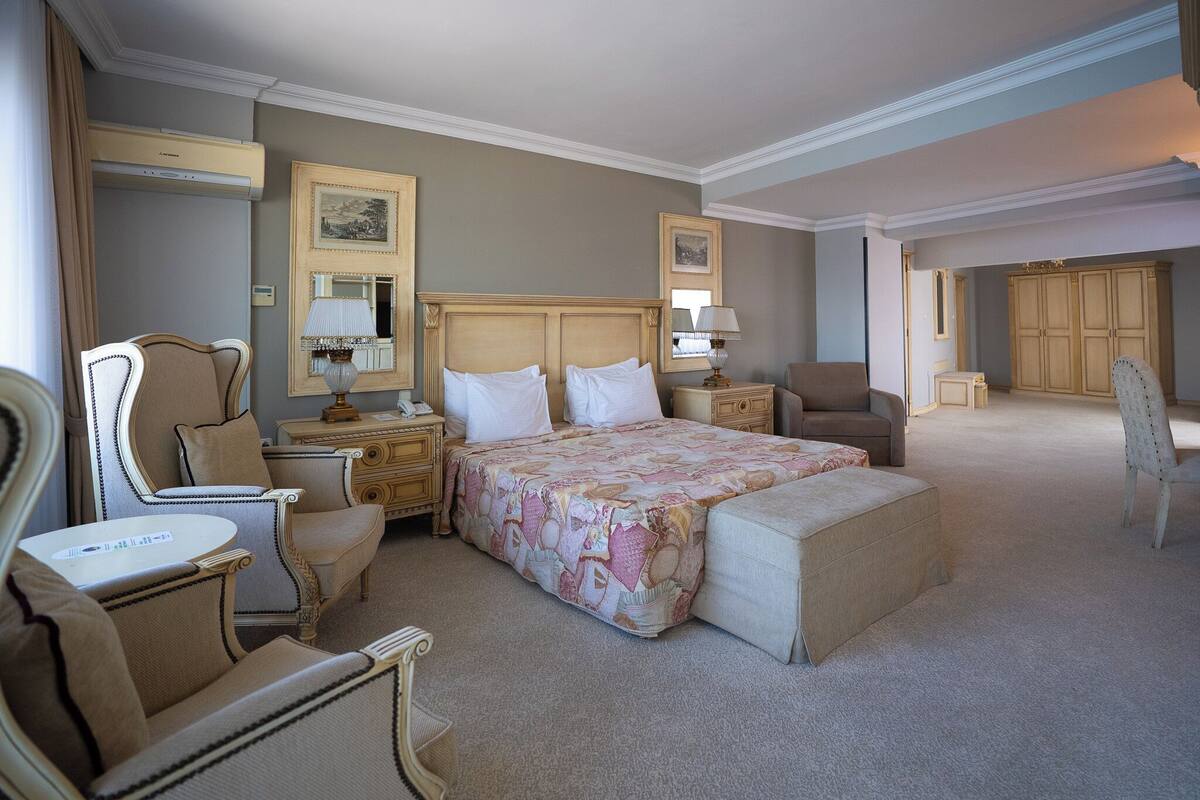 Una habitación de hotel con una cama grande, dos mesitas de noche, una silla, un escritorio y un armario.