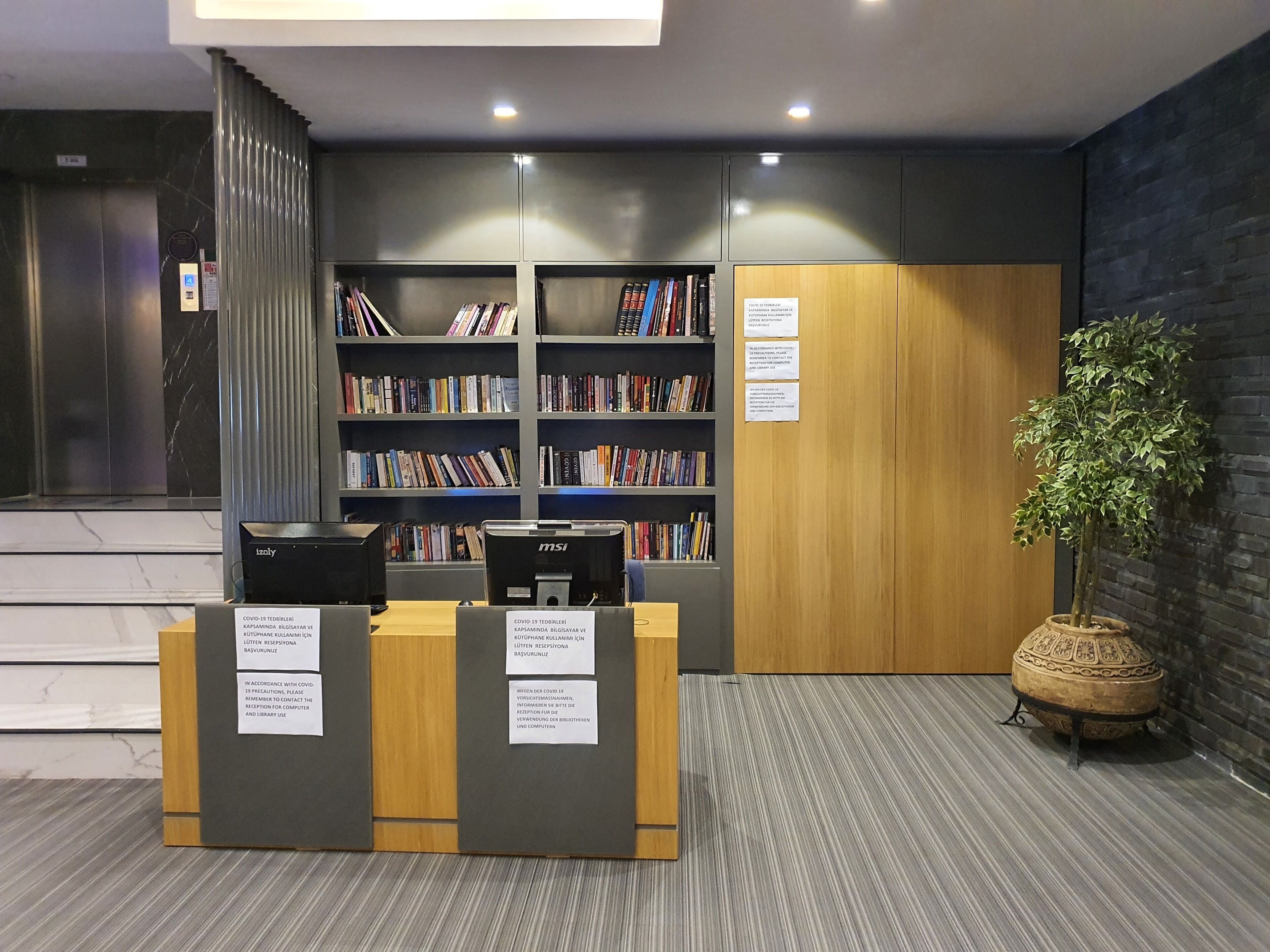 A modern library with bookshelves, a reception desk, and a potted plant.
