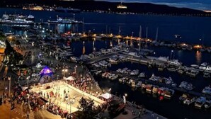 A marina at night with boats docked, a crowd gathering, and a stage with lights. - Akol Hotel (Çanakkale)