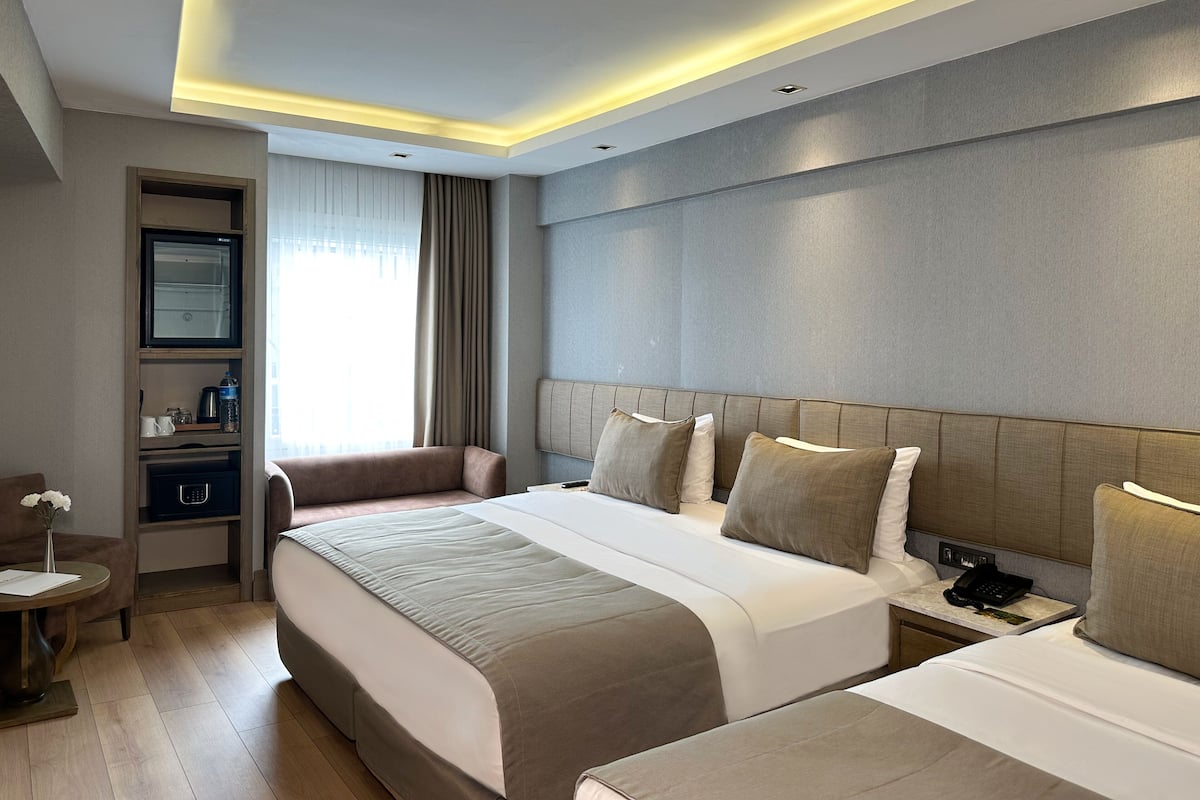 A hotel room with a large bed, a bedside table, a nightstand, a built-in shelf, and a window with curtains.