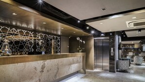A modern reception area with a marble counter, geometric wall design, and a central elevator. - AHC Grand Bazaar Hotel (Istanbul)