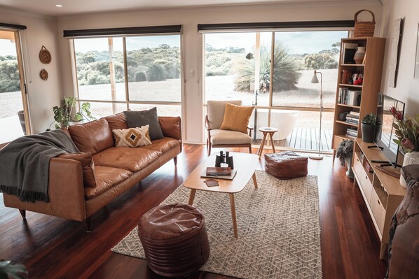 A spacious living room with a leather sofa, a small coffee table, and a bookshelf.