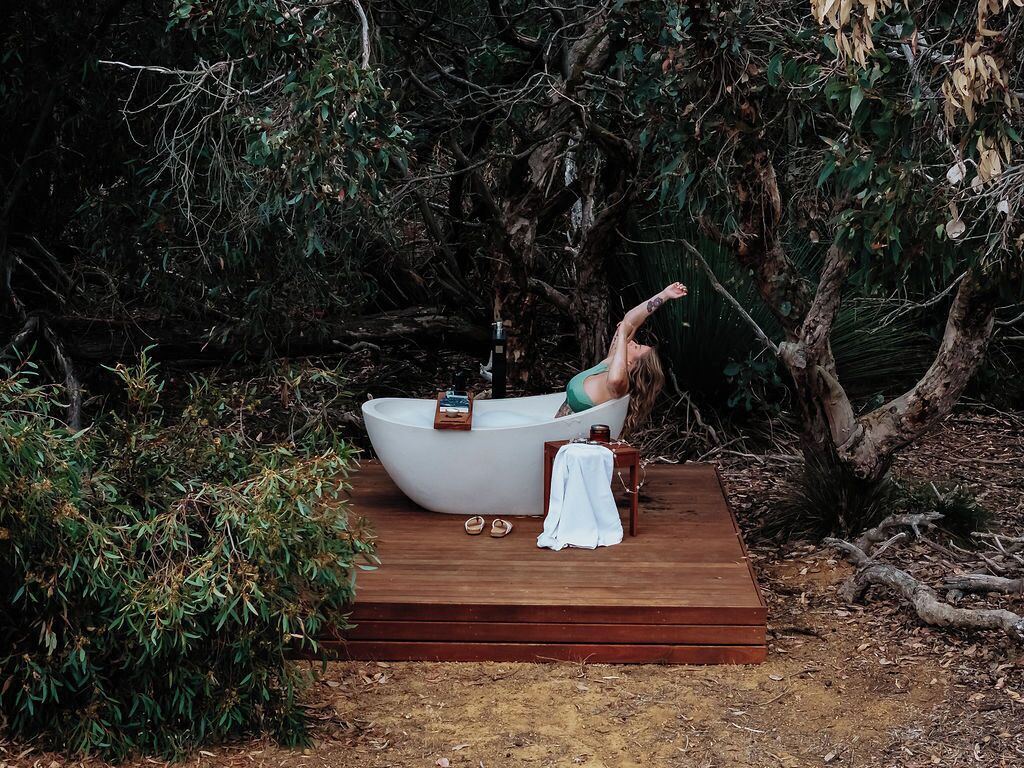 A bathtub on a wooden platform surrounded by dense foliage.