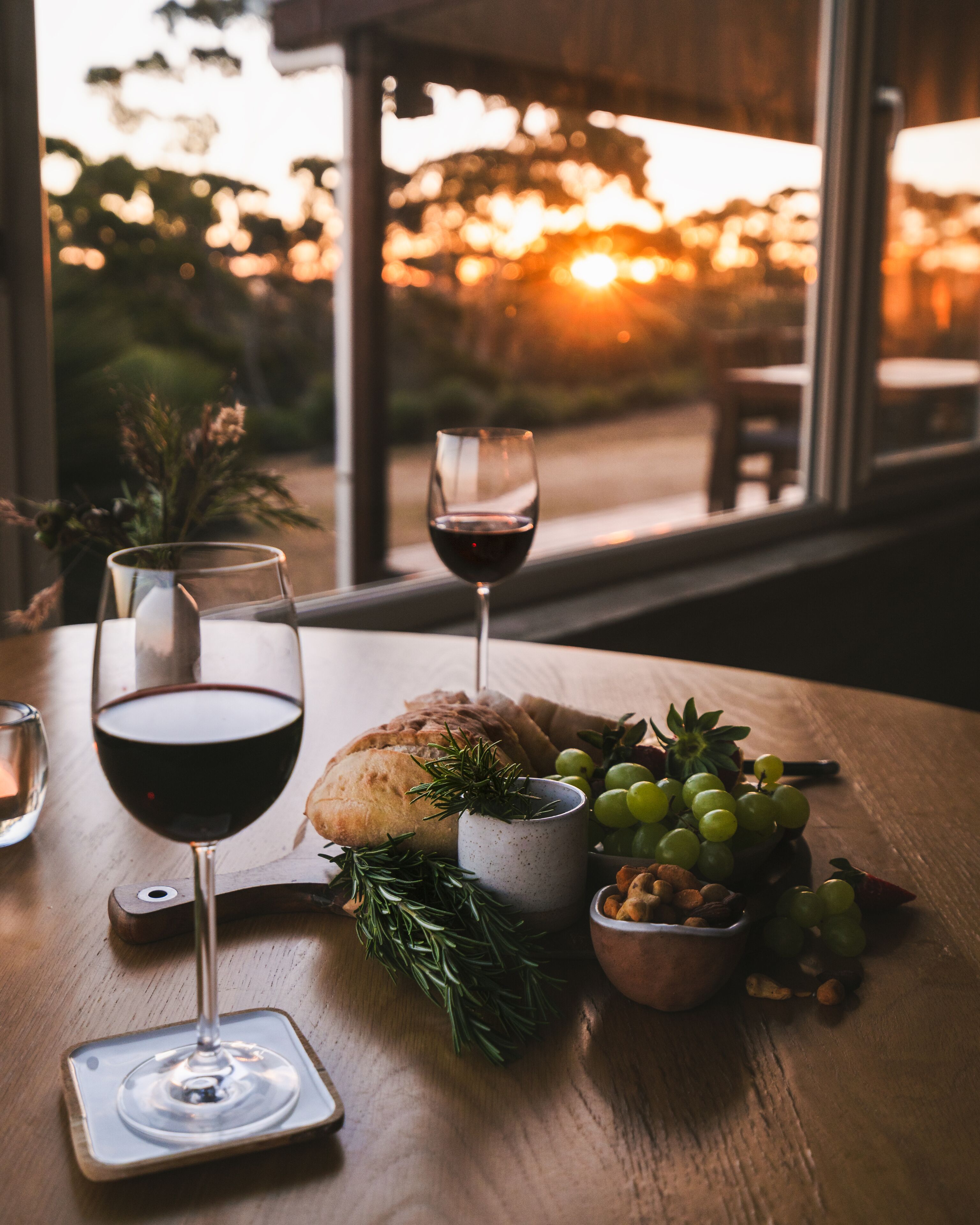 A table with a glass of red wine, a loaf of bread, a bowl of grapes, and a small bowl of nuts.