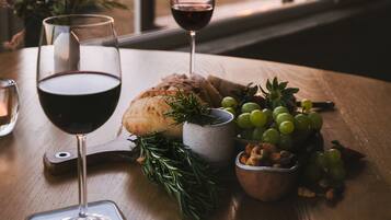 A table with a glass of red wine, a loaf of bread, a bowl of grapes, and a small bowl of nuts.