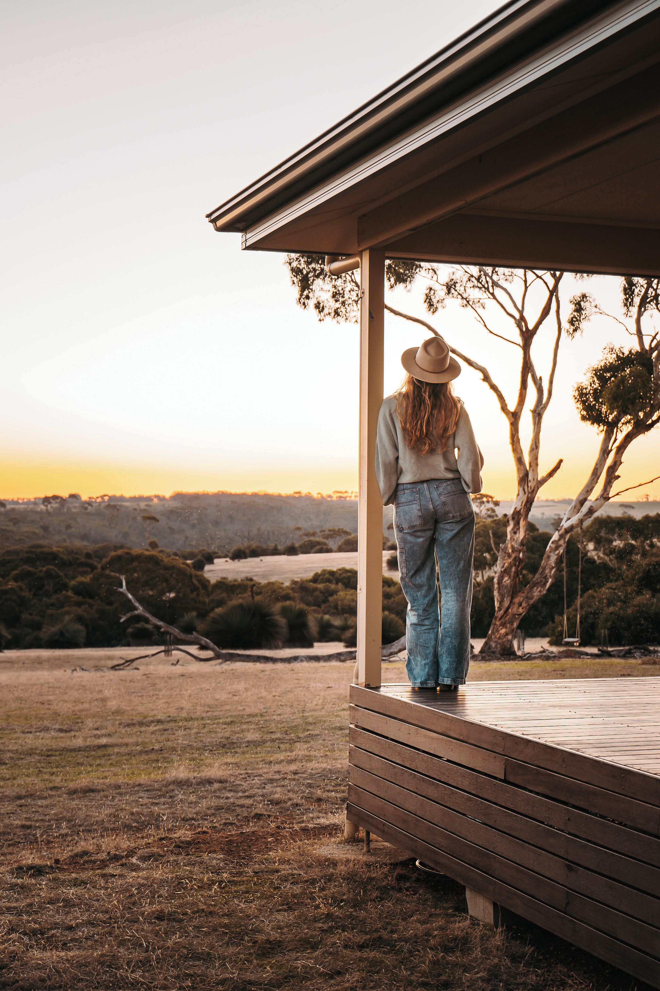 Une personne se tient sur une terrasse en bois, d’où l’on peut admirer un paysage et des arbres.