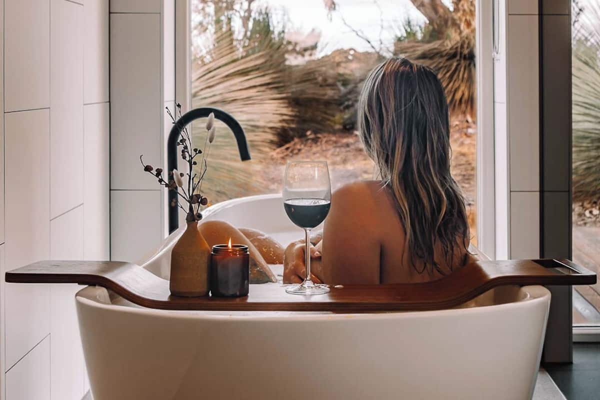 A person relaxing in a bathtub with a view of trees outside.