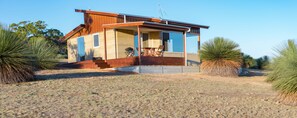 A modern house with a large glass window, a wooden deck, and a patio area. - Ecopia Retreat (Seddon)