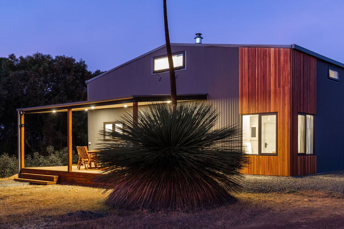 A modern house with a large glass door, a wooden deck, and a well-lit interior.