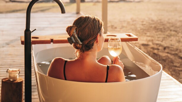 A woman in a large bathtub with a view of a beach and trees in the background.