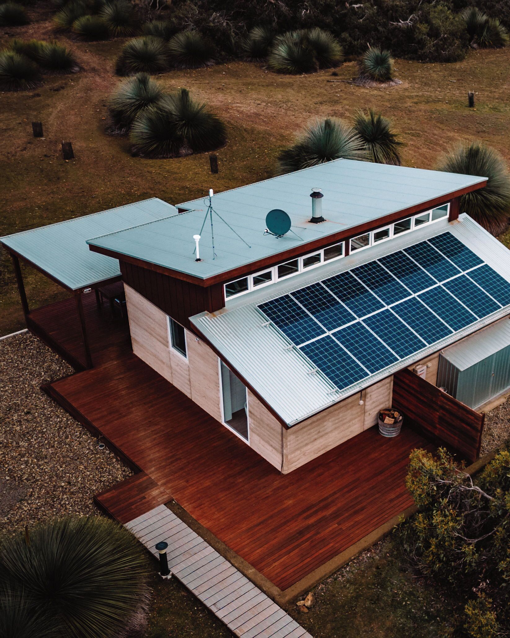 A modern house with a solar panel roof, a covered patio, and a wooden deck.
