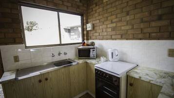 A kitchen with wooden cabinets, a microwave, a kettle, and a window with a view of a building outside.