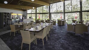 A spacious indoor dining area with high ceilings and large windows, wicker furniture, and a bar area with a display of bottles. - Mannum Motel (Mannum)