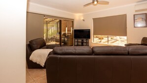 A living room with a brown leather sofa, a flat-screen TV, and a sliding glass door leading to an outdoor area. - Mannum Motel (Mannum)
